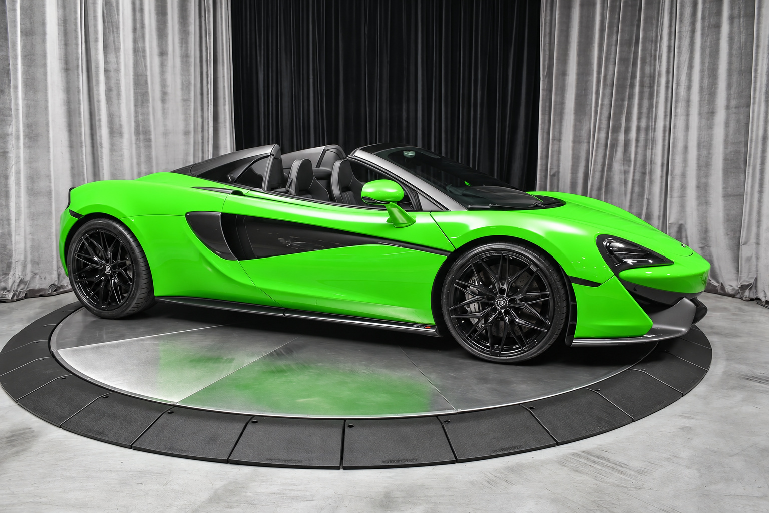 Side profile of the Mantis Green McLaren 570S Spider, roof down, black wheels, on a studio turntable