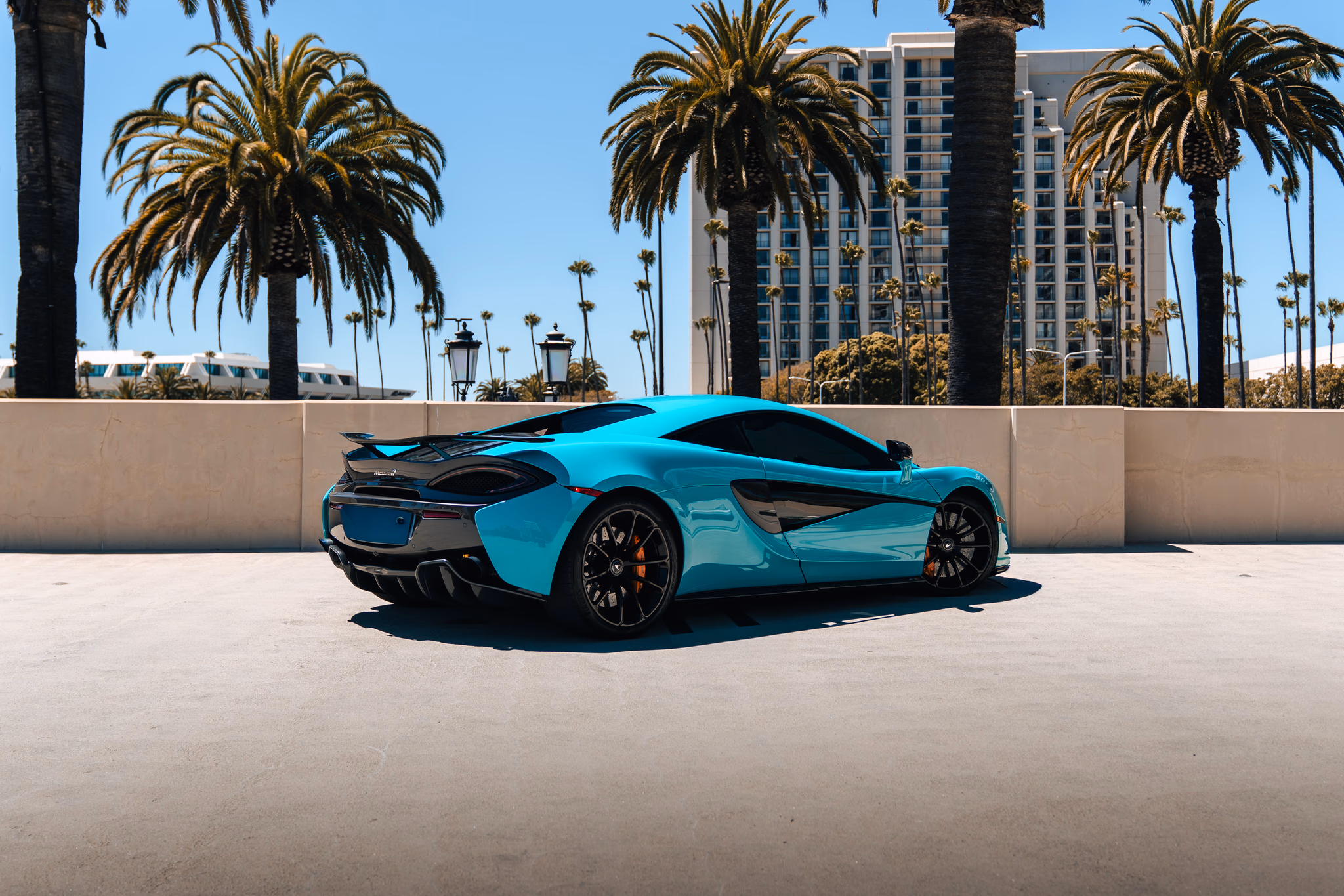 Rear three-quarter of the Curacao Blue McLaren 570S coupe, rear deck and twin exhausts, palms behind