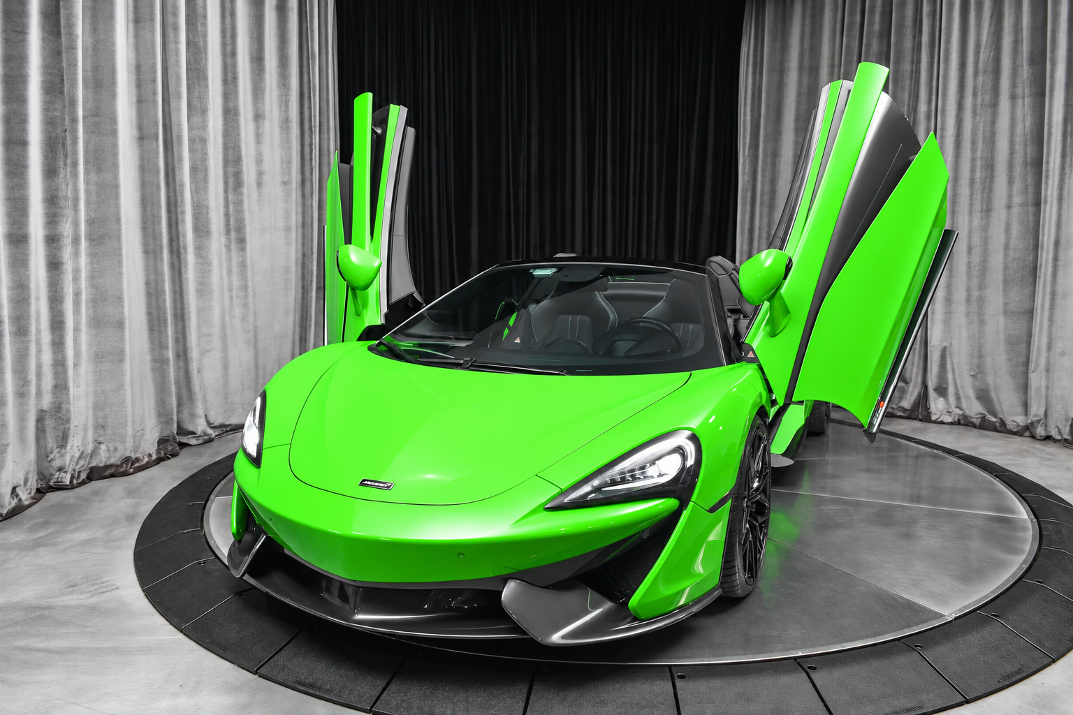 Mantis Green McLaren 570S Spider with both dihedral doors raised and the roof folded, on a studio turntable