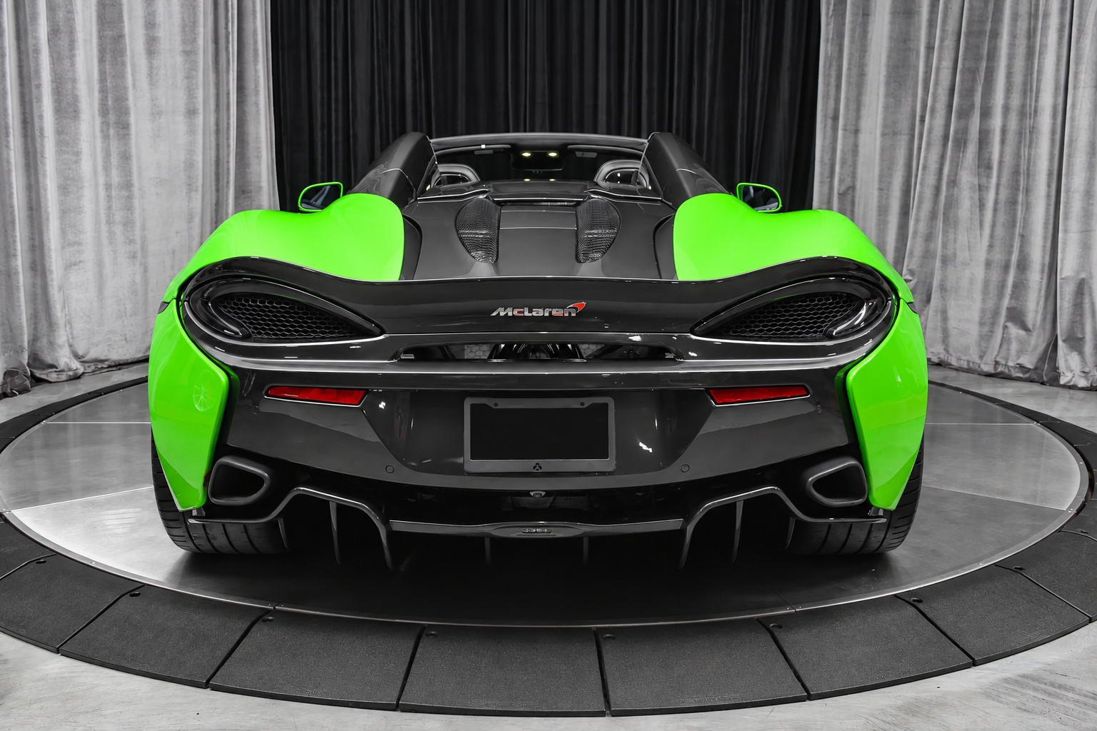 Straight rear view of the green 570S Spider showing the twin high exhausts, rear mesh and black buttresses