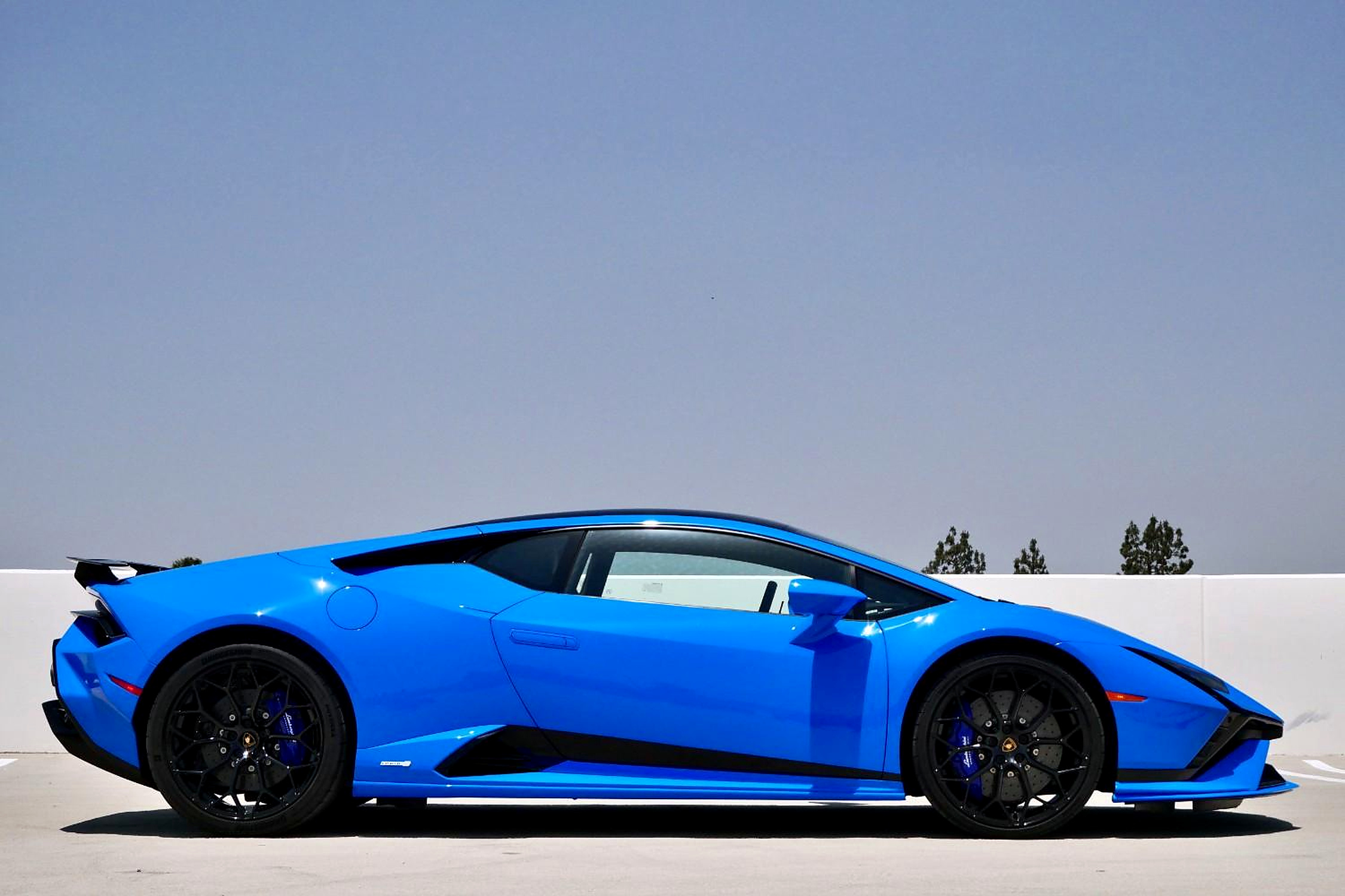 Side profile of the bright blue Huracan Tecnica showing the fixed rear wing and black wheels on a rooftop
