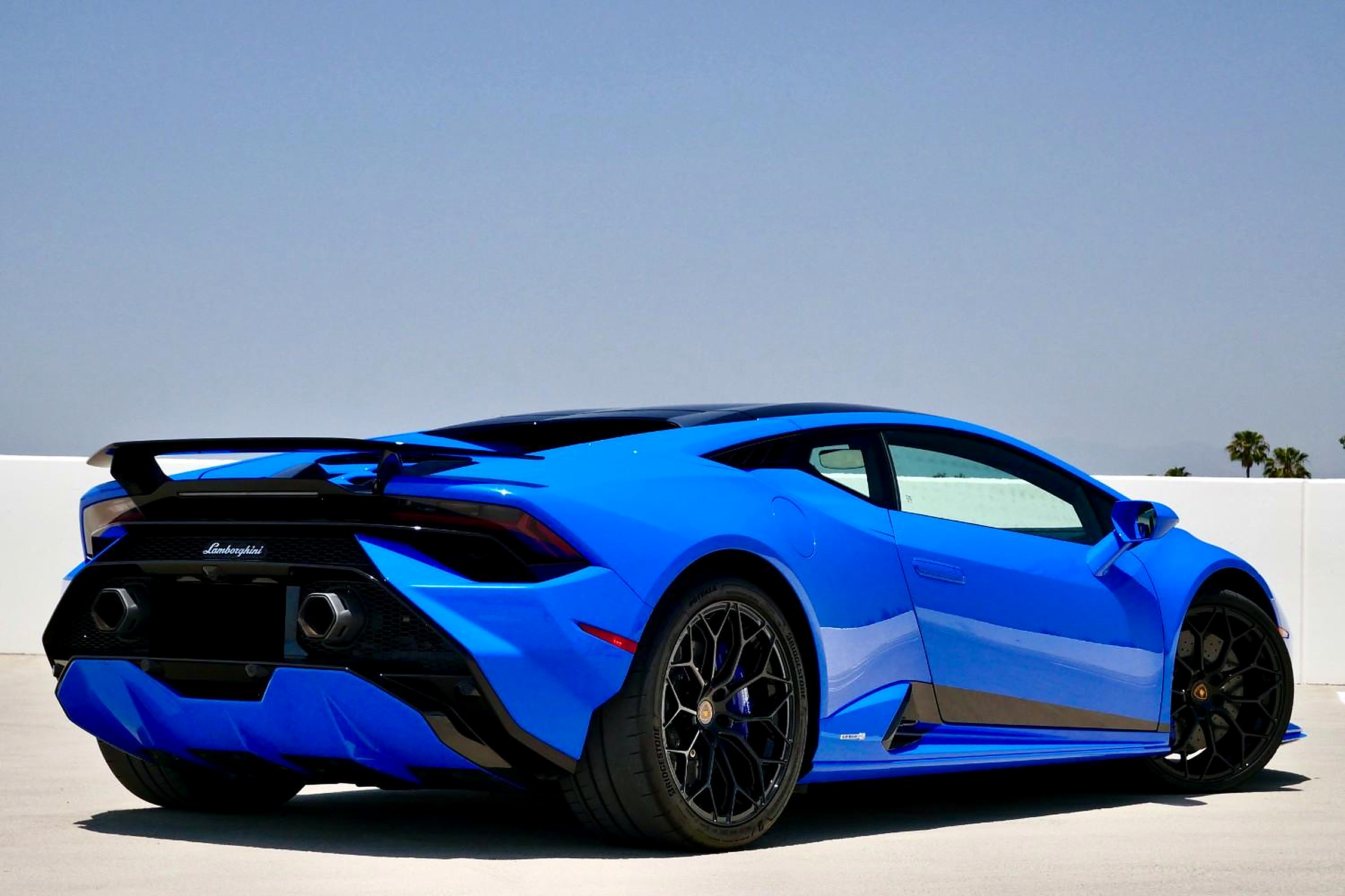 Rear three-quarter of the Blu Le Mans Huracan Tecnica with the fixed wing against a clear sky