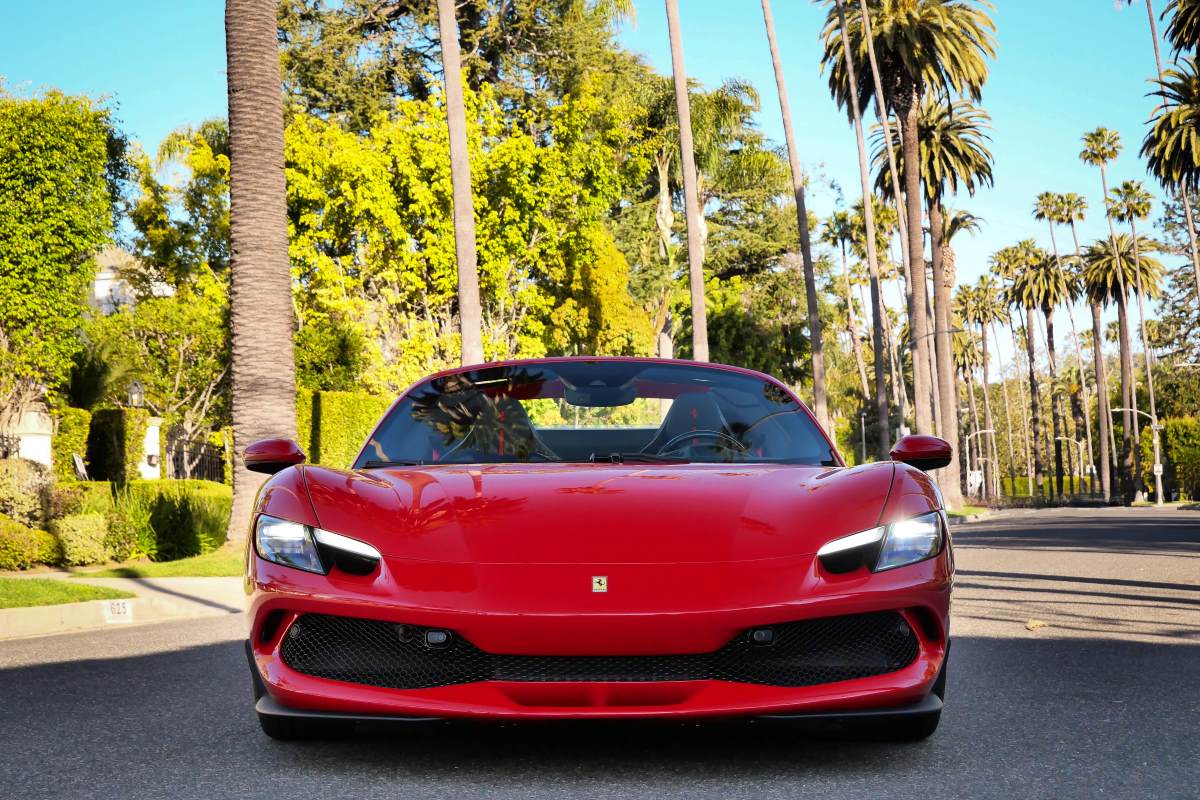 Head-on view of the red 296 GTS with its headlights on, tall palms lining the Beverly Hills street behind