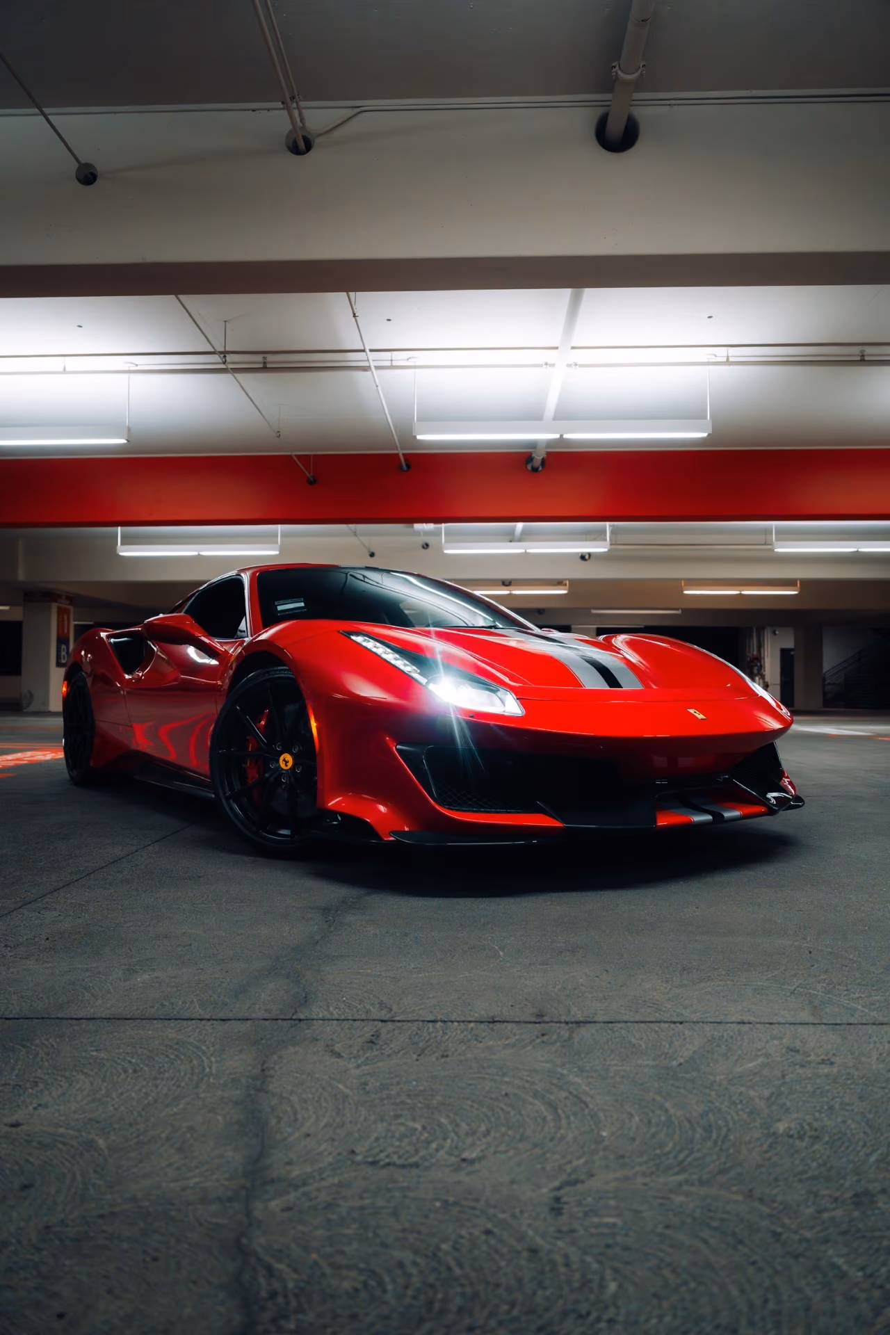 Front view of the red 488 Pista under the lights of an underground garage, the stripe running over the nose