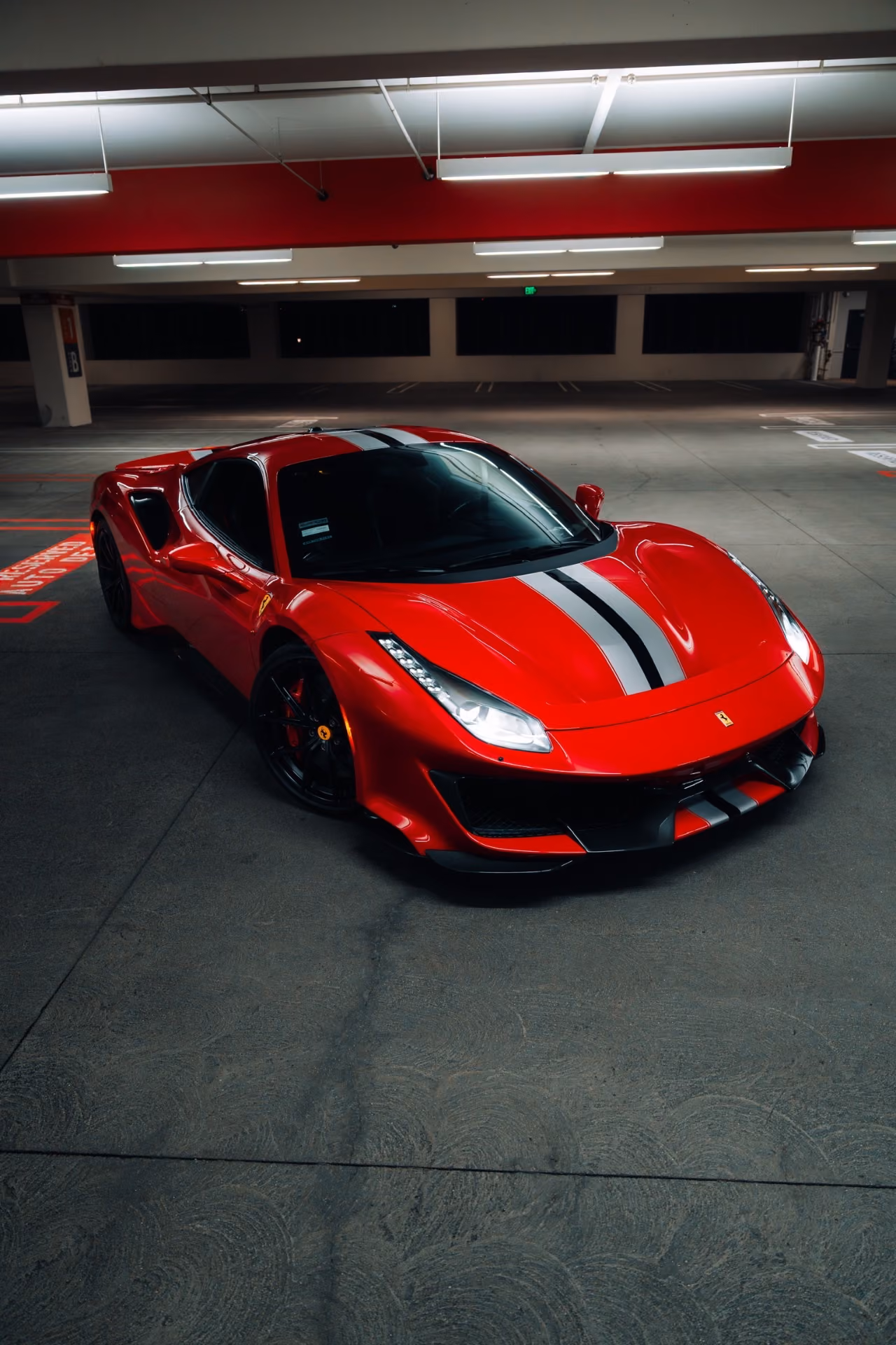 Low head-on shot of the red Ferrari 488 Pista in a garage with red painted walls, stripe pointing at the lens