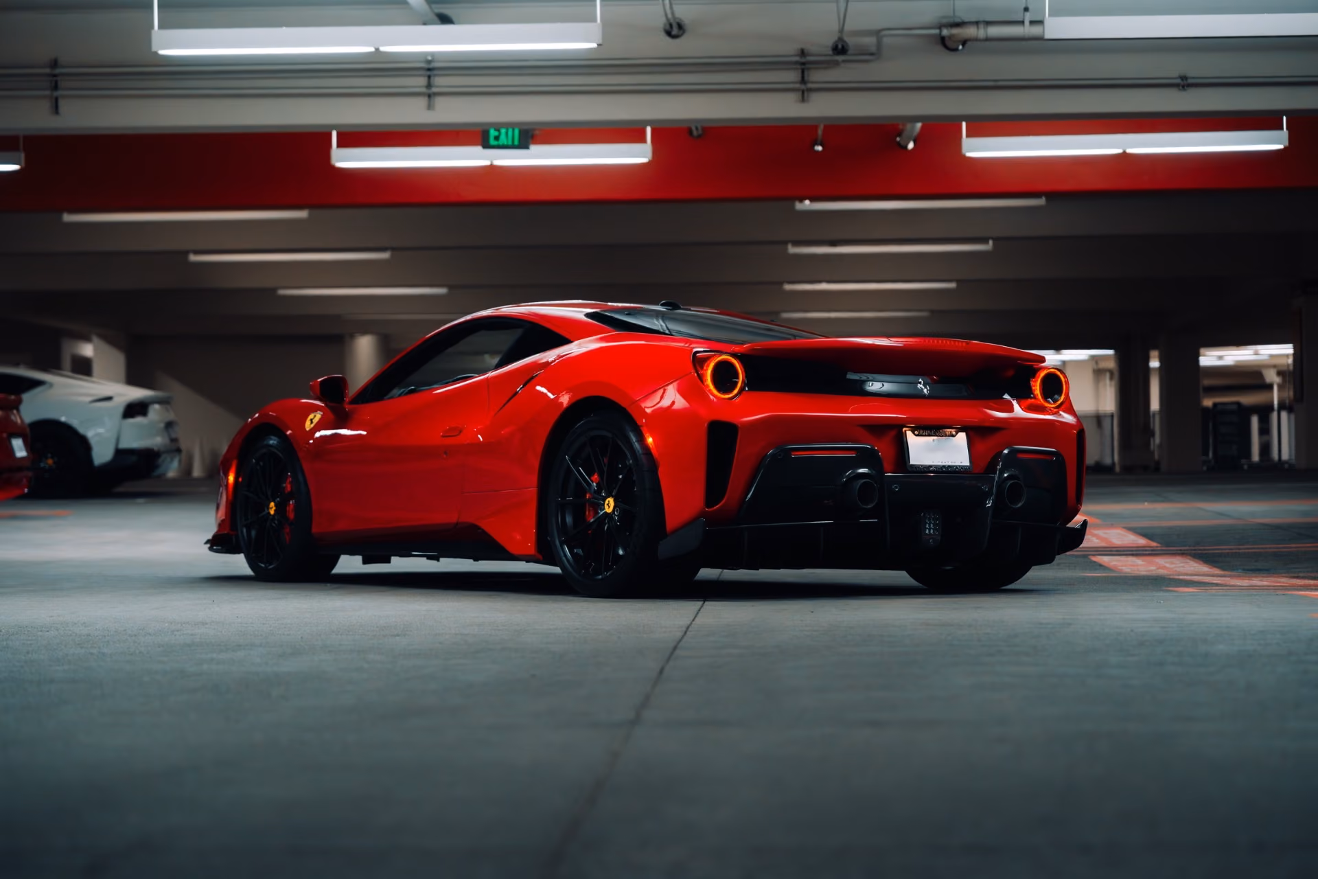 Rear three-quarter of the red 488 Pista on black wheels in an underground garage, round tail lights lit