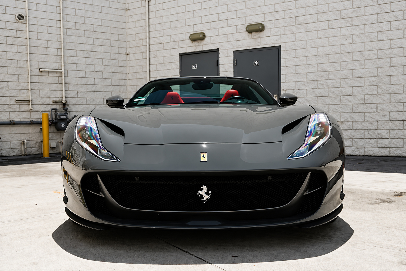 Head-on view of the grey Ferrari 812 GTS, roof stowed, red seats visible above the windscreen