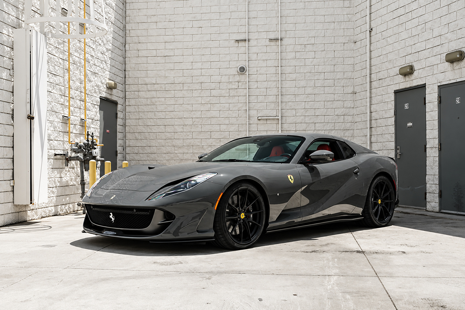 Grey Ferrari 812 GTS with the roof down and a red interior, front three-quarter view against a white block wall