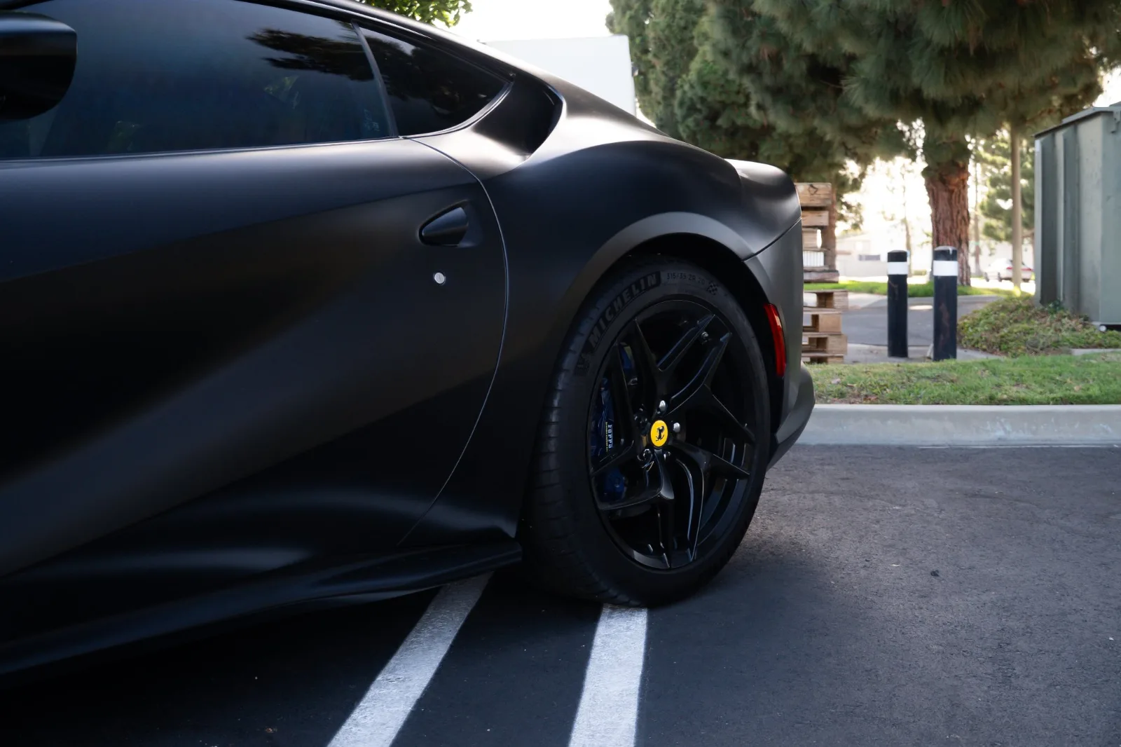 Rear wheel and flank of the satin black Ferrari 812 Superfast in an office park parking space
