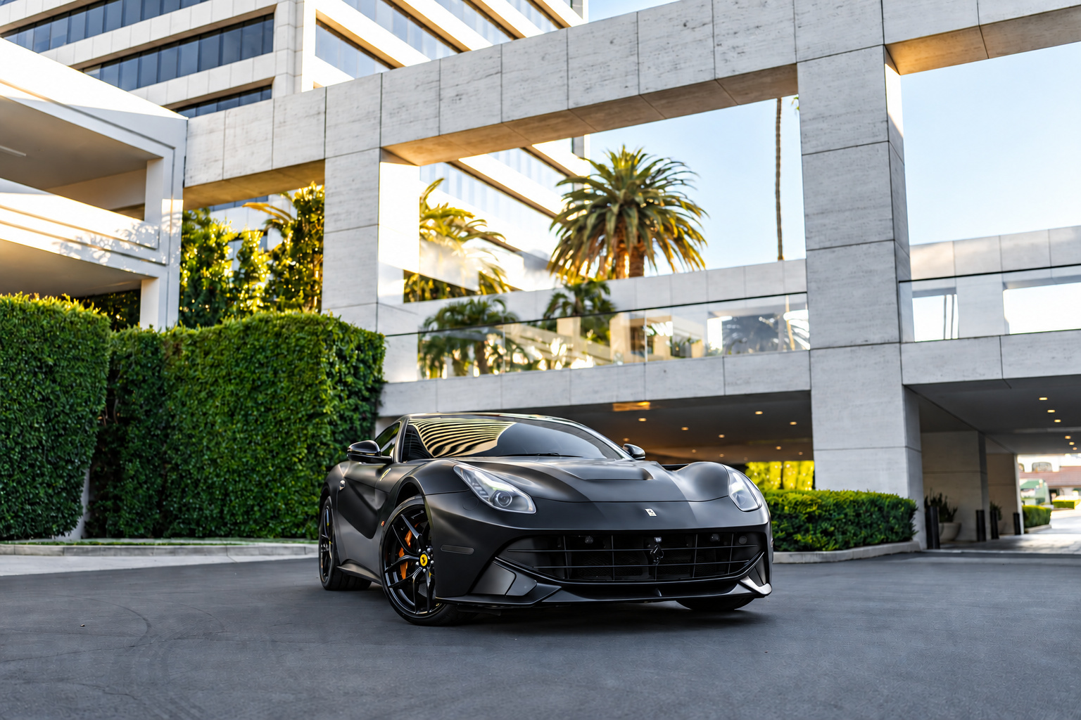 Head-on view of the satin black Ferrari F12berlinetta under a hotel entrance canopy