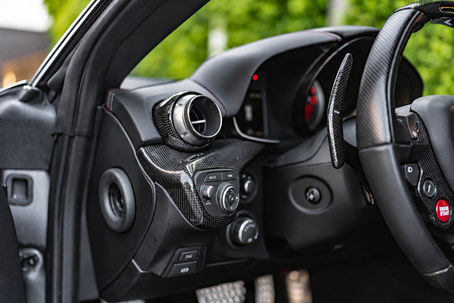 Driver's side of the Ferrari F12berlinetta cabin with the carbon steering wheel, red paddle and carbon dash vents