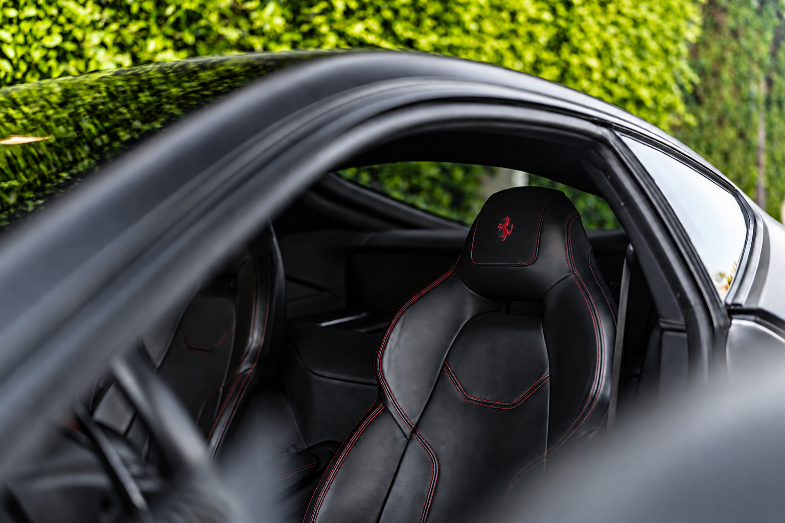 Black seat of the Ferrari F12berlinetta with red stitching and the Cavallino in the headrest, through the open door