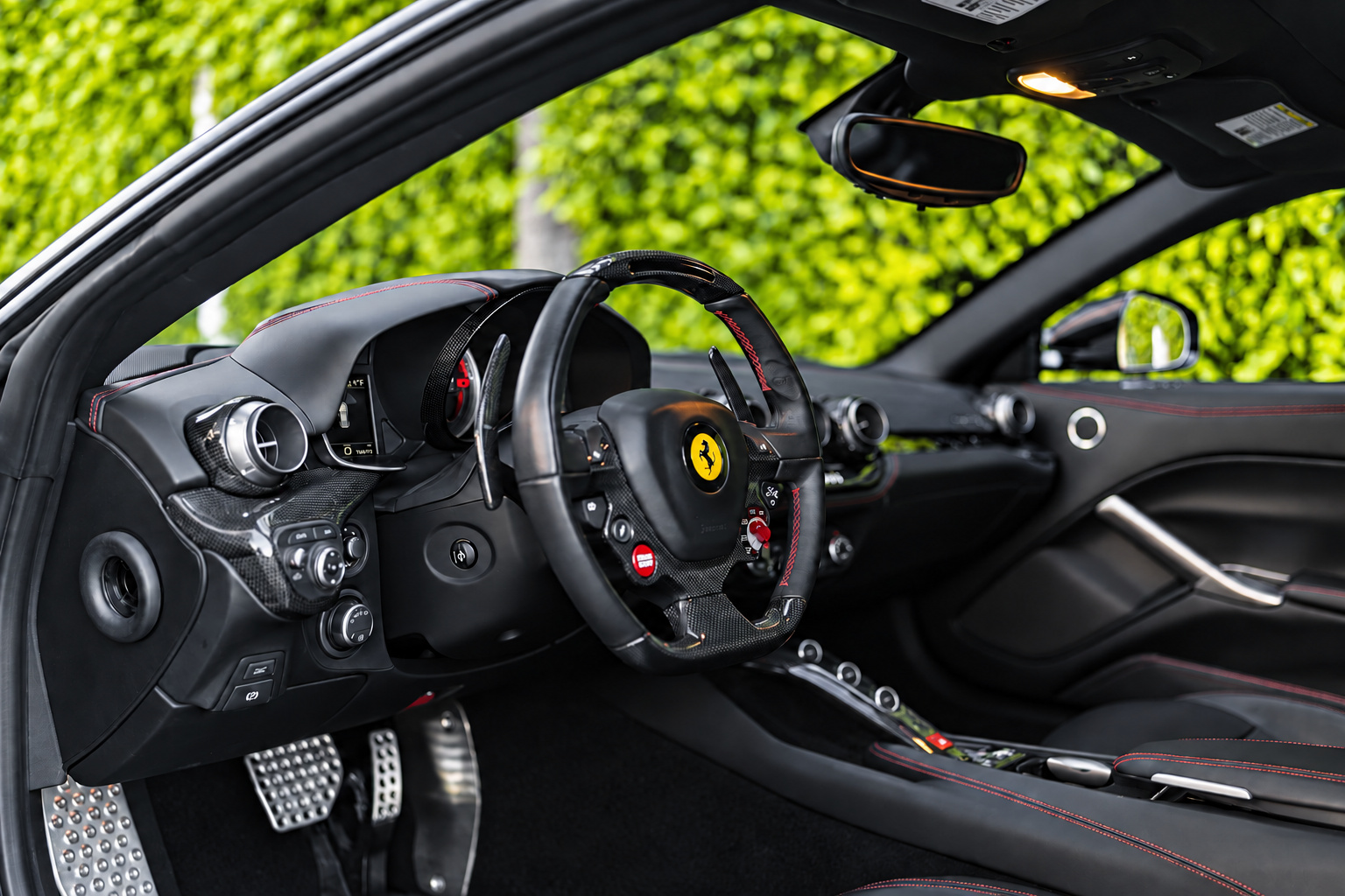 Inside the satin black Ferrari F12berlinetta, black leather with red stitching, the steering wheel and the pedals
