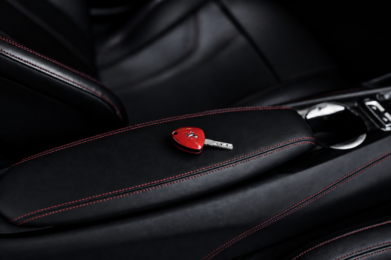 Red Ferrari key resting on the black leather armrest of the F12berlinetta, red stitching along the seam