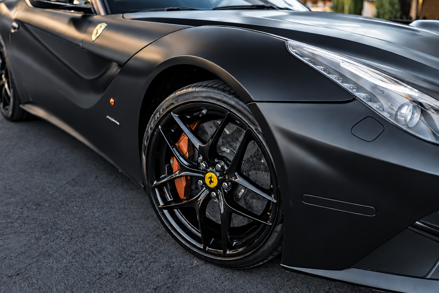 Front wheel of the Ferrari F12berlinetta in black with a yellow brake caliper, satin black fender above