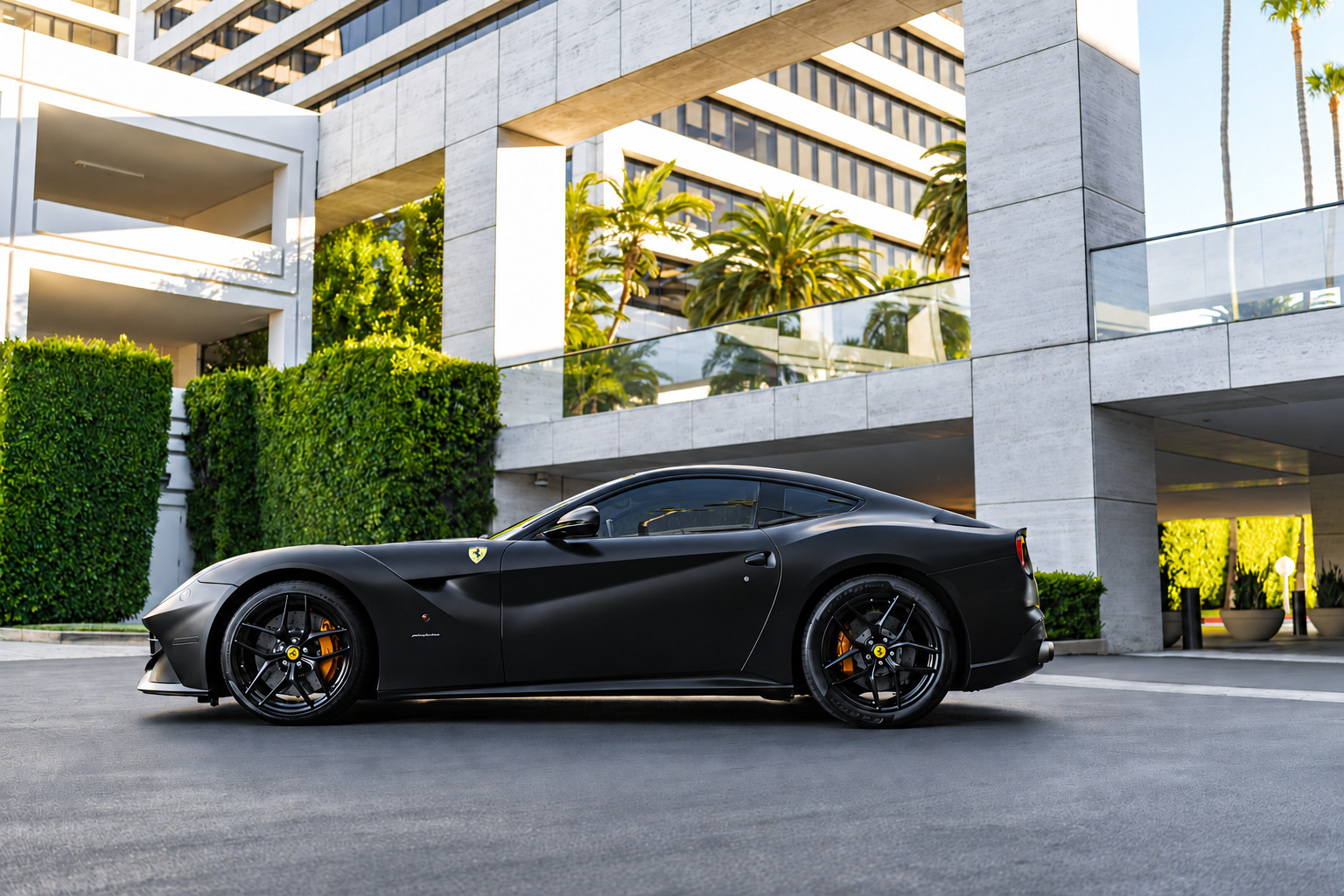 Side profile of the satin black Ferrari F12berlinetta on black wheels in front of a hotel entrance