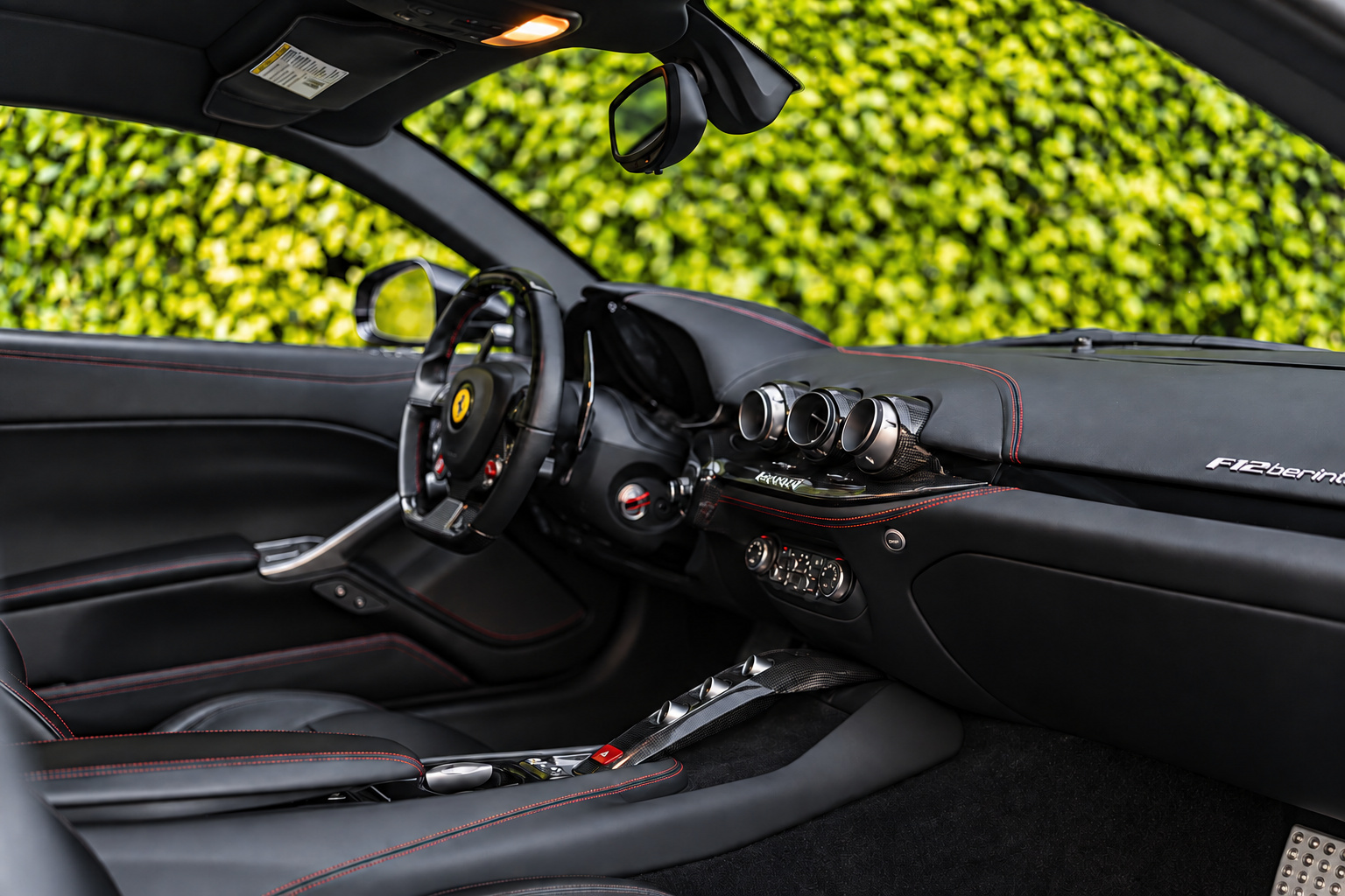 Driver's view across the Ferrari F12berlinetta cabin, black leather dash, carbon steering wheel and the door panel