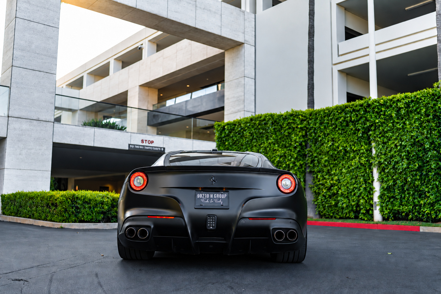 Rear view of the satin black Ferrari F12berlinetta with its quad exhaust tips beside a green hedge