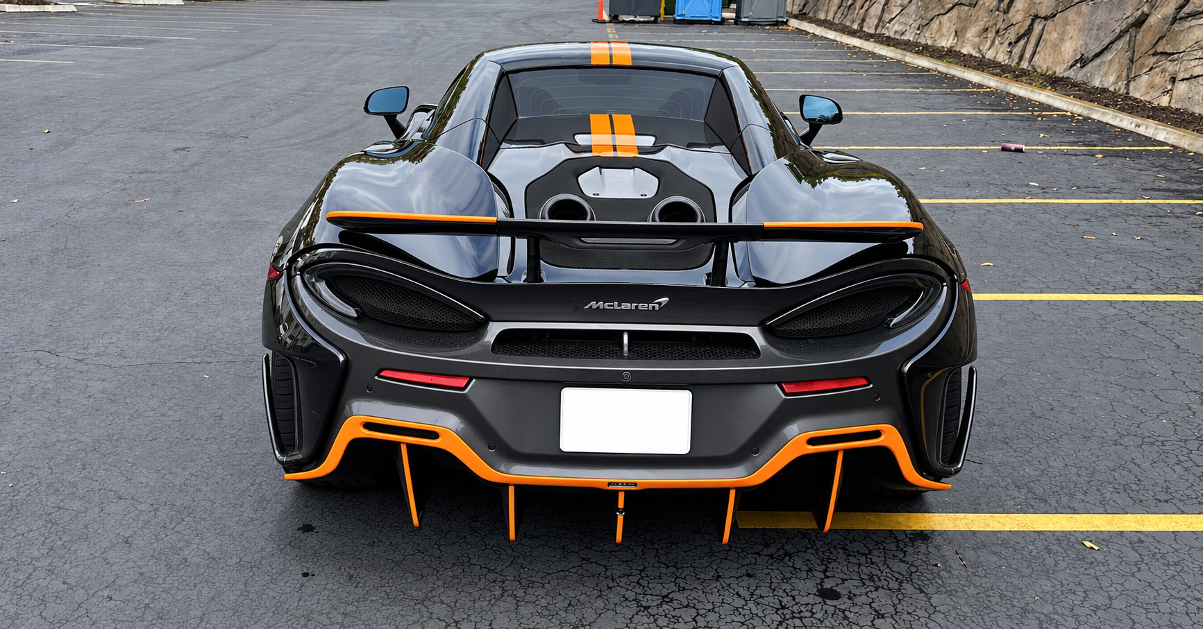 Straight rear view of the black McLaren 600LT Spider showing the fixed wing, top-exit exhausts and orange deck stripes