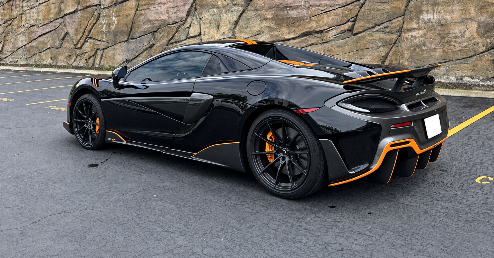 Rear three-quarter of the black McLaren 600LT Spider with the orange diffuser accent and fixed rear wing, roof down