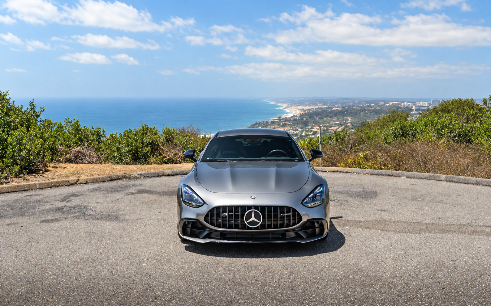 Head-on view of the silver AMG GT 43 showing the Panamericana grille, coastline and ocean behind