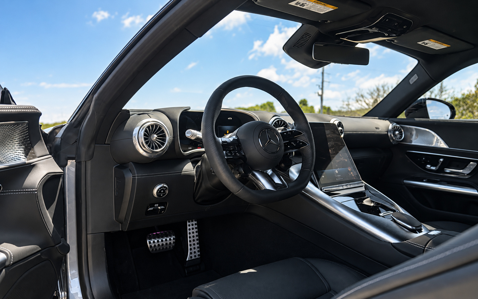 Driver's side of the AMG GT 43 cabin with the flat-bottomed AMG steering wheel, aluminum pedals and digital cluster