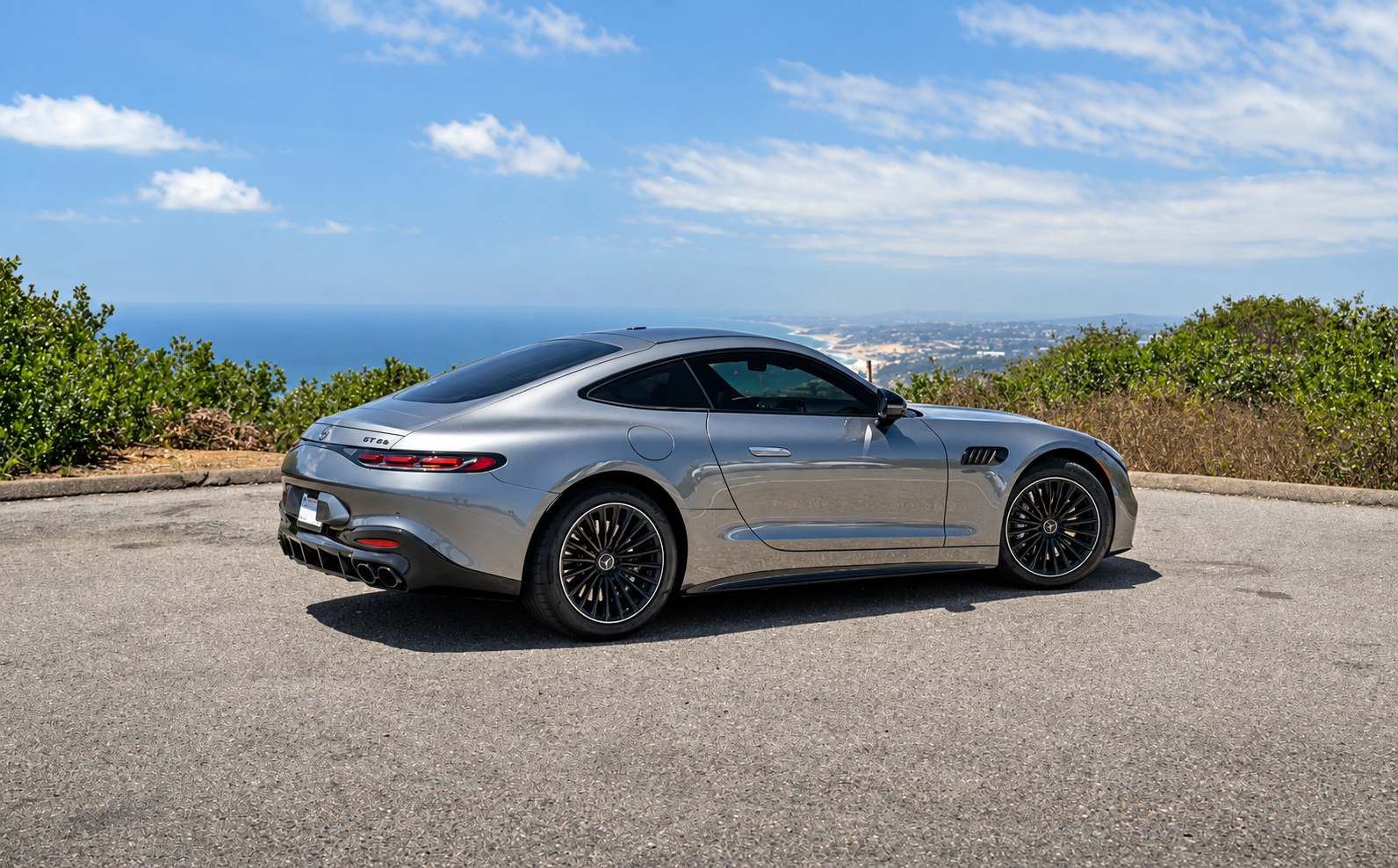 Rear three-quarter of the Hightech Silver AMG GT 43 on black wheels, Pacific coastline below the overlook