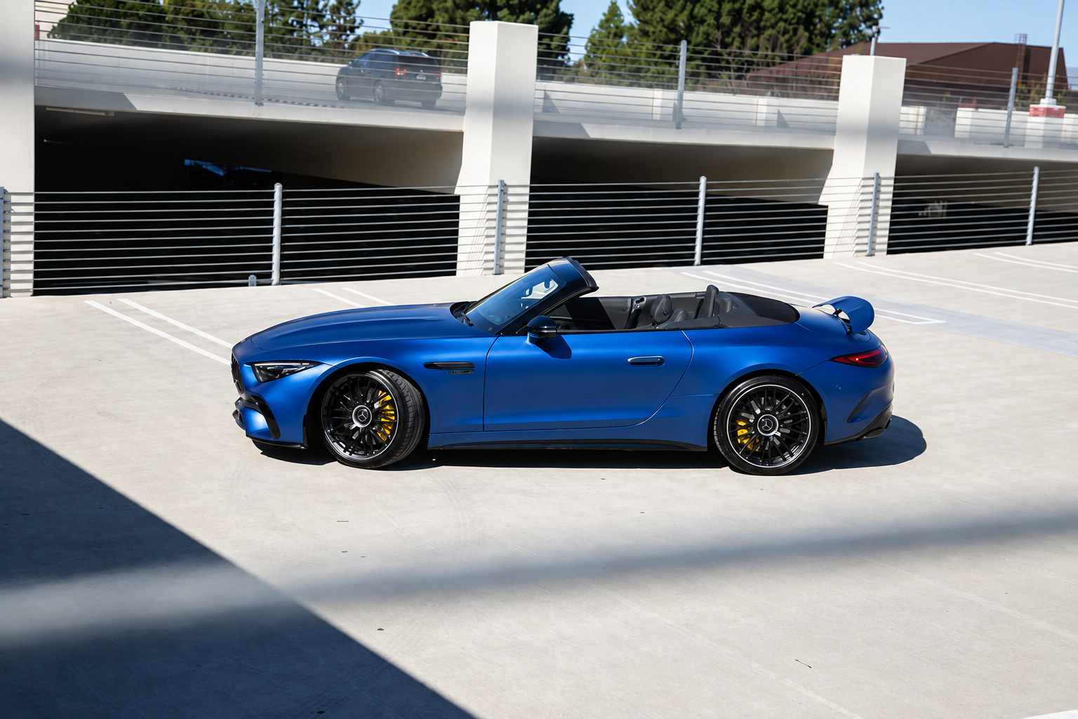 Wide side three-quarter of the blue Mercedes-Benz AMG SL rental, roof folded, parked on a rooftop deck