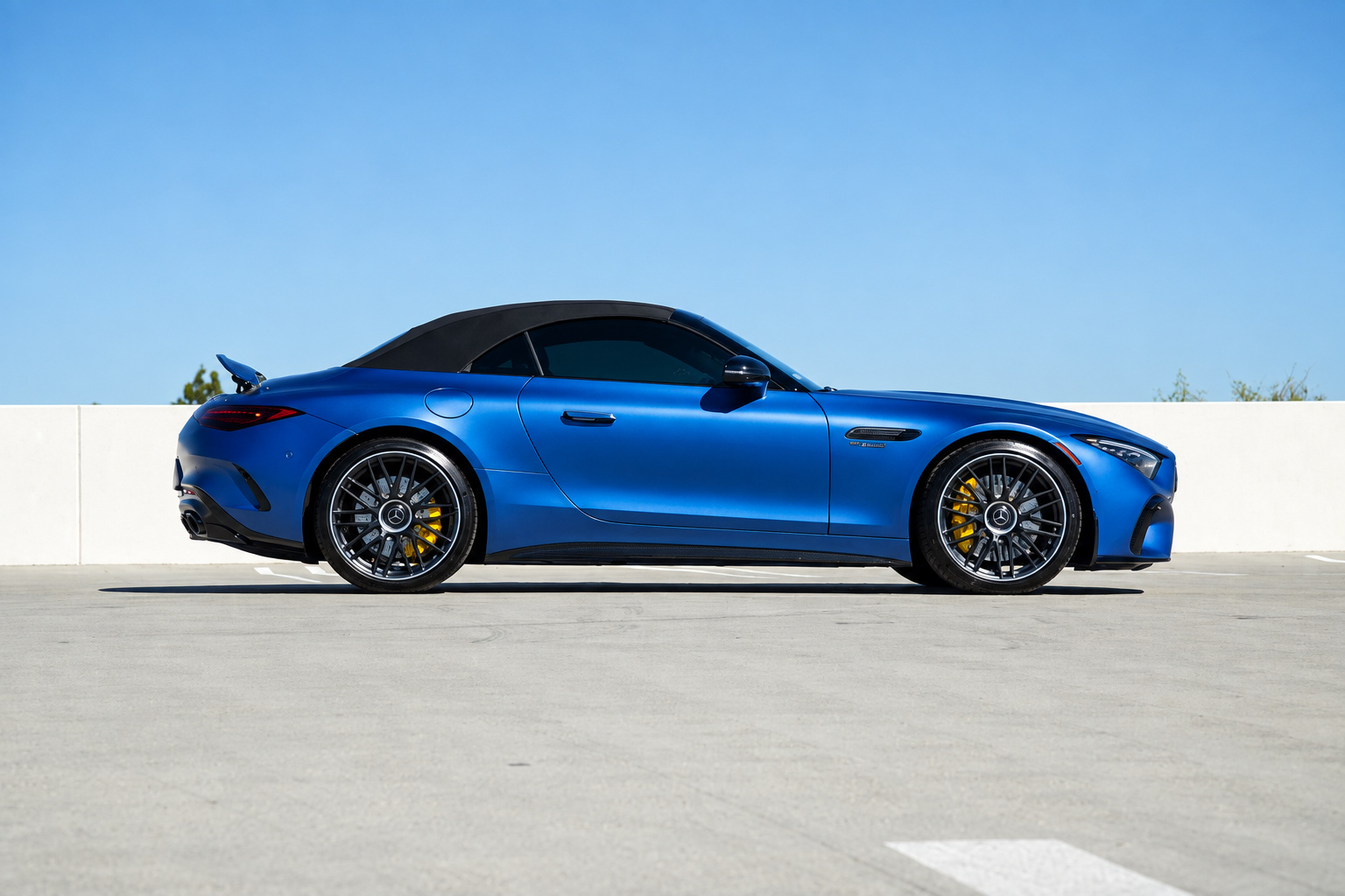 Side profile of the blue Mercedes-Benz AMG SL rental with the black soft top up and yellow calipers