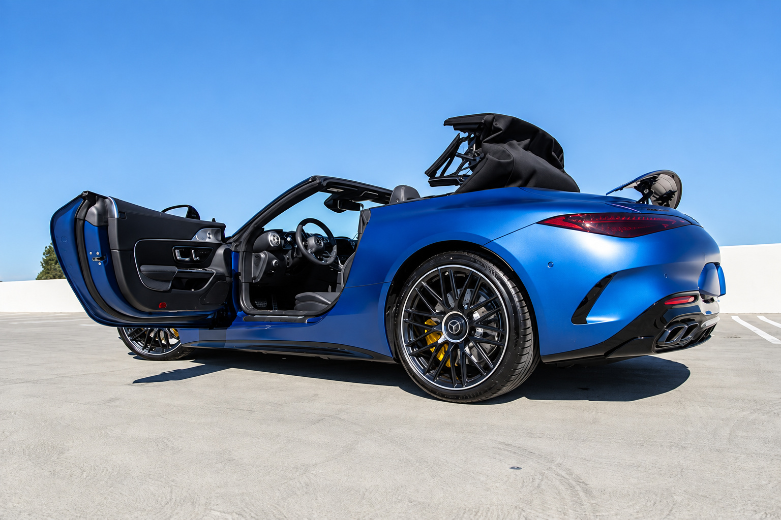 Rear three-quarter of the blue Mercedes-Benz AMG SL rental with the door open and the soft top mid-fold