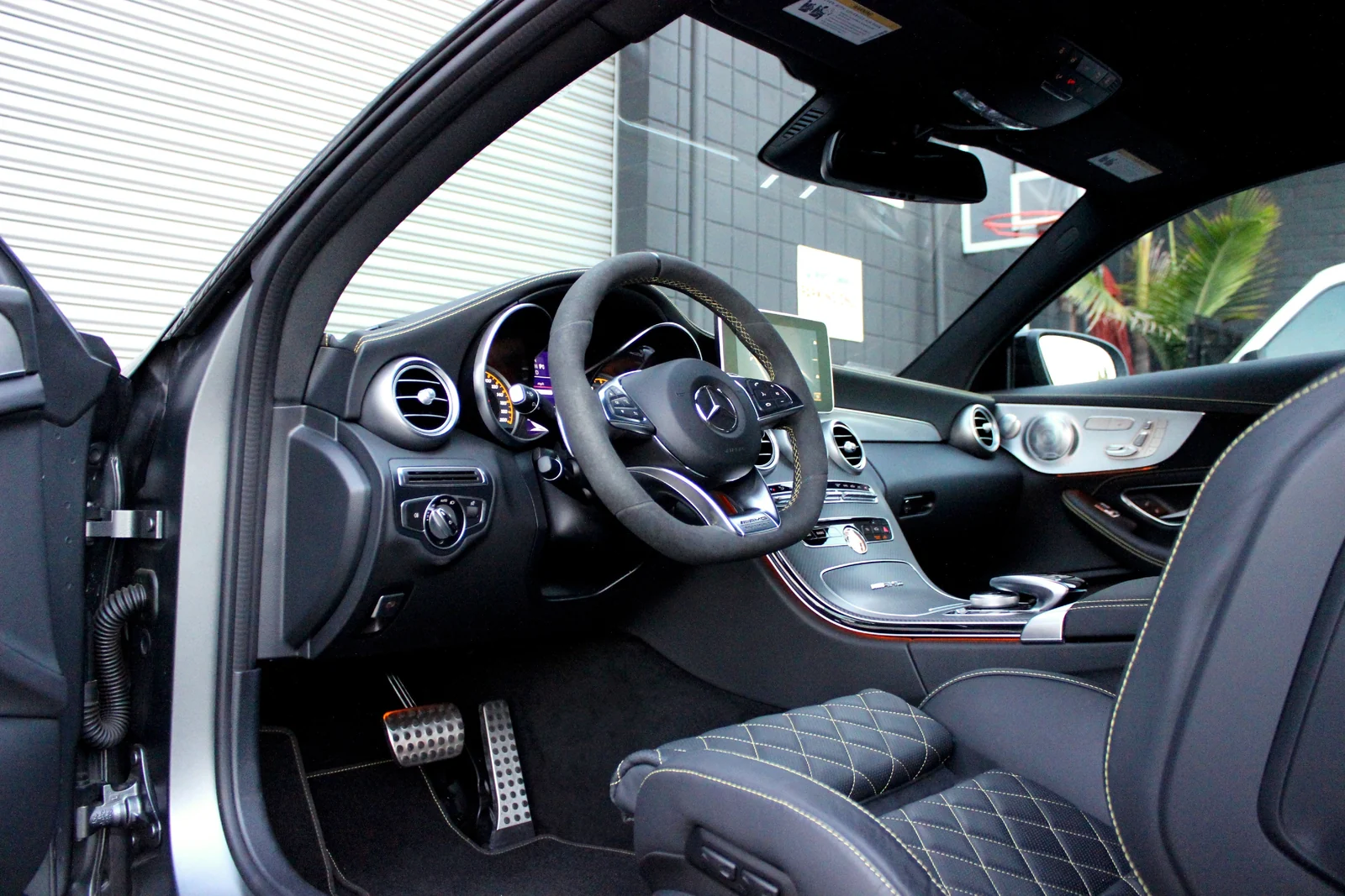 Door open on the grey Mercedes-Benz AMG C63 rental, quilted black seat with yellow stitching and AMG pedals