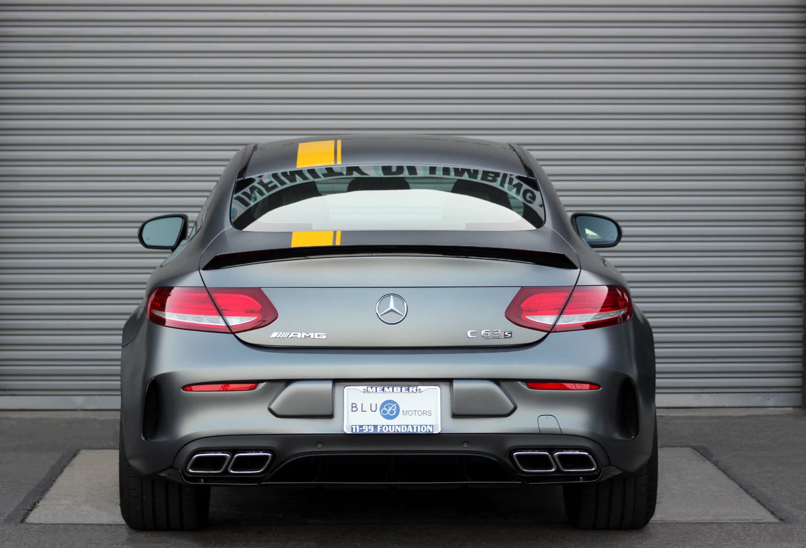 Rear view of the matte grey Mercedes-Benz AMG C63 rental, yellow roof stripe and quad exhaust tips
