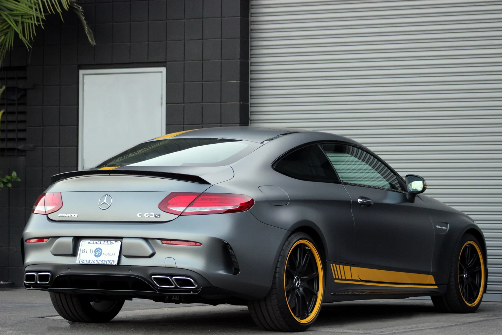 Rear three-quarter of the matte grey Mercedes-Benz AMG C63 rental, yellow sill stripe and black wheels