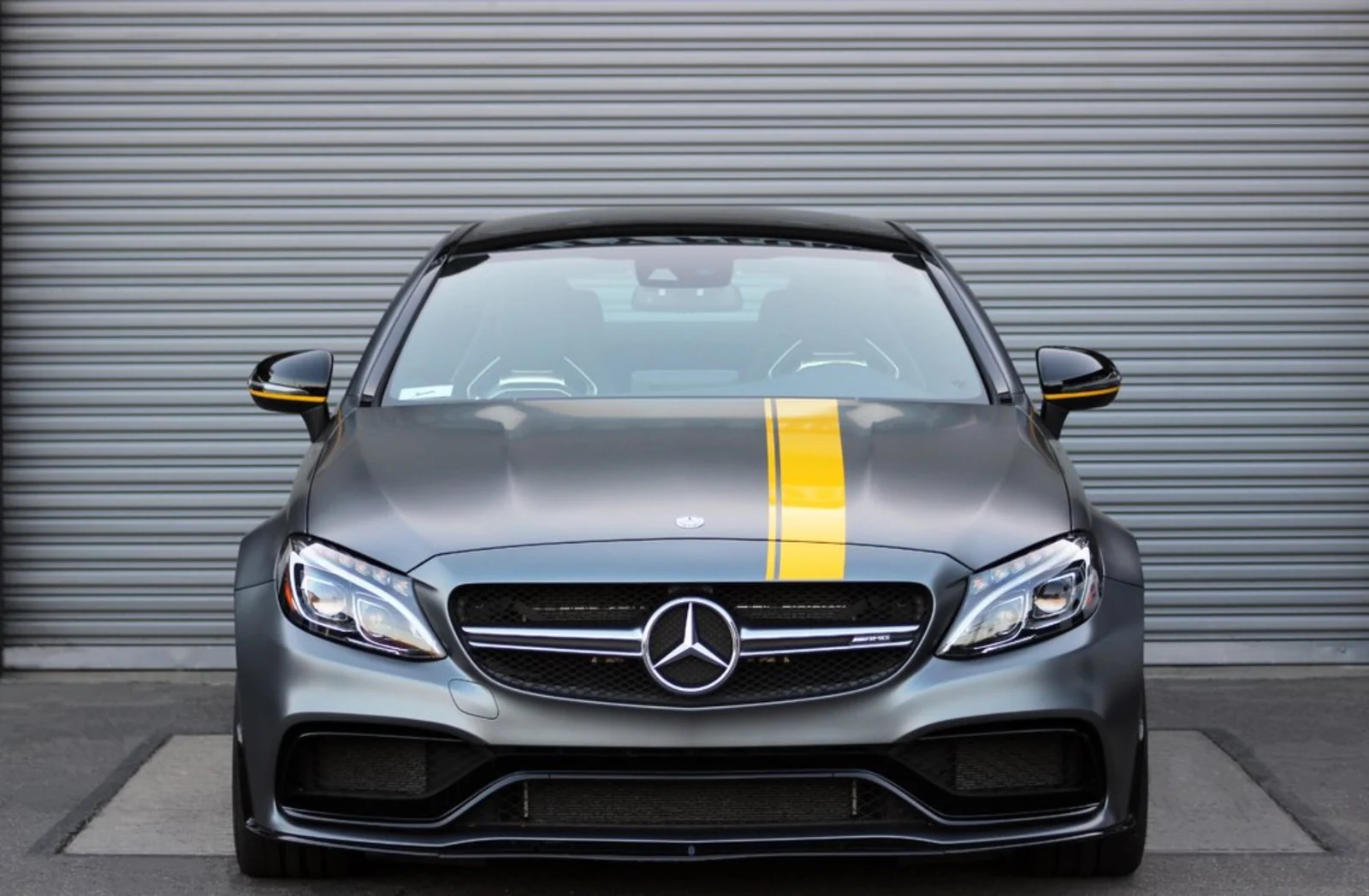 Head-on view of the grey Mercedes-Benz AMG C63 rental, the yellow stripe running up the hood to the roof