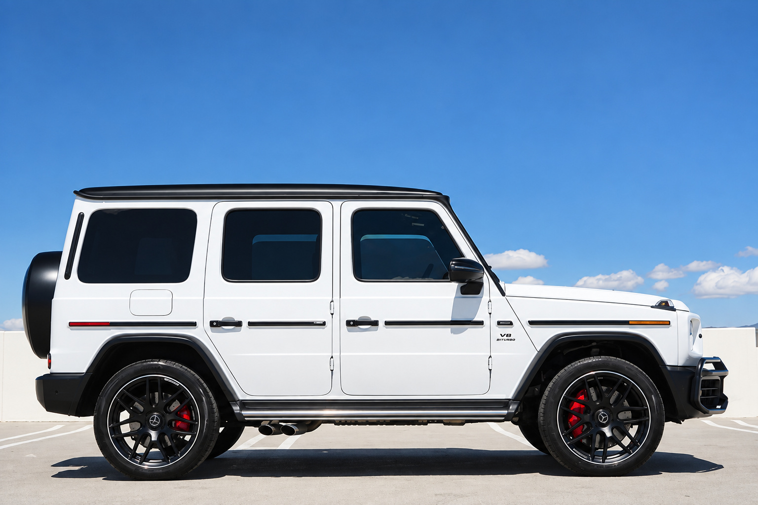 Side profile of the white AMG G63 with the black roof, black wheels and red brake calipers on a rooftop deck