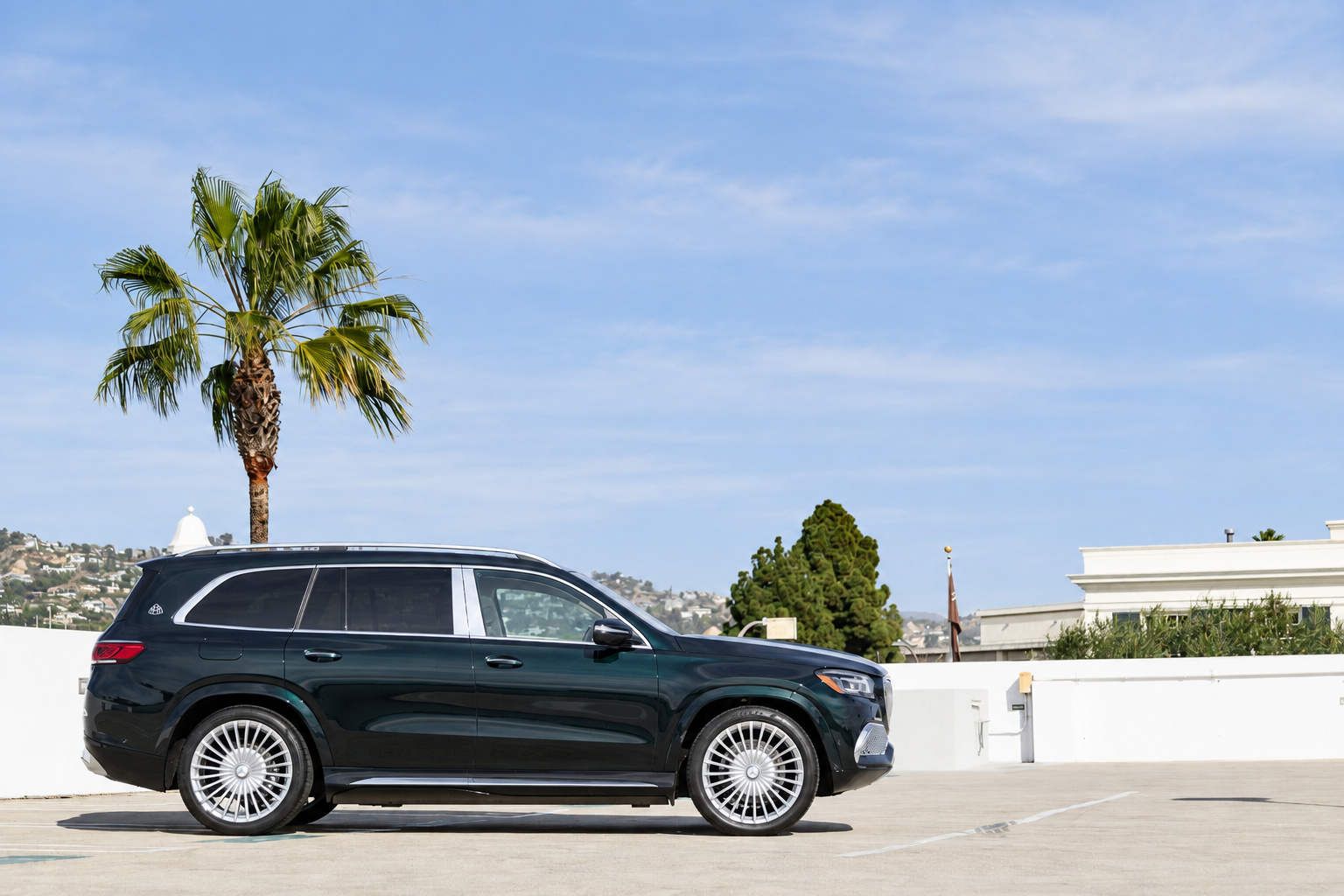 Side profile of the Emerald Green Maybach GLS 600 on a rooftop deck in Beverly Hills with a palm and the tower behind