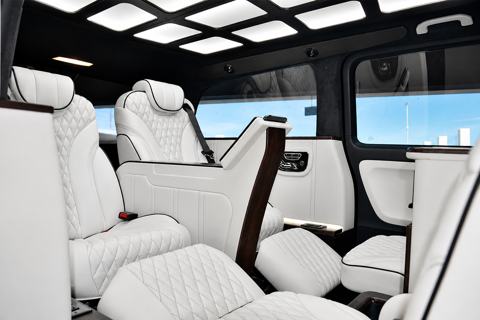 Rear cabin of the Mercedes-Benz Metris rental, white quilted captain chairs, wood console and lit ceiling