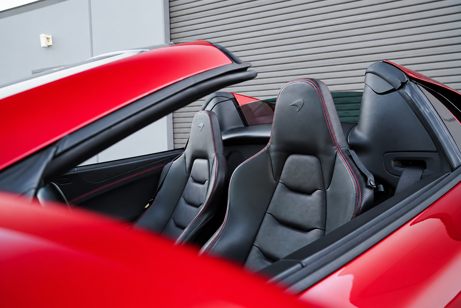 Black leather seats with red stitching inside the red McLaren 650S Spider, roof folded, red deck behind