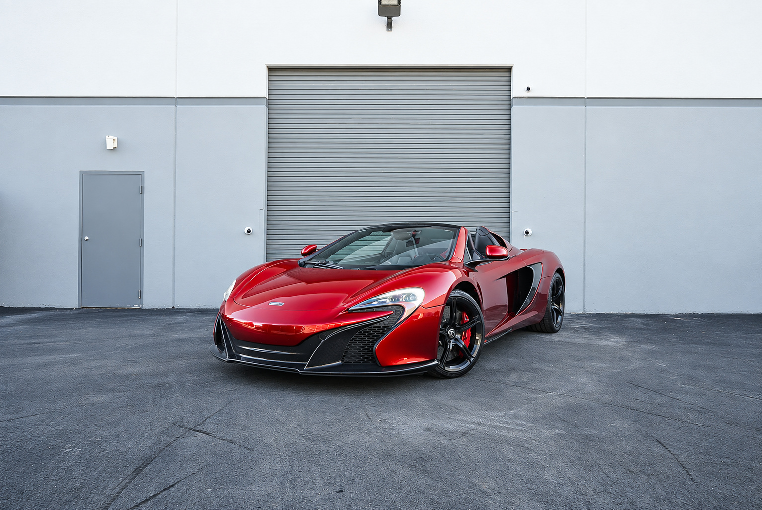 Front three-quarter of the Volcano Red McLaren 650S Spider, roof down, black wheels and red calipers