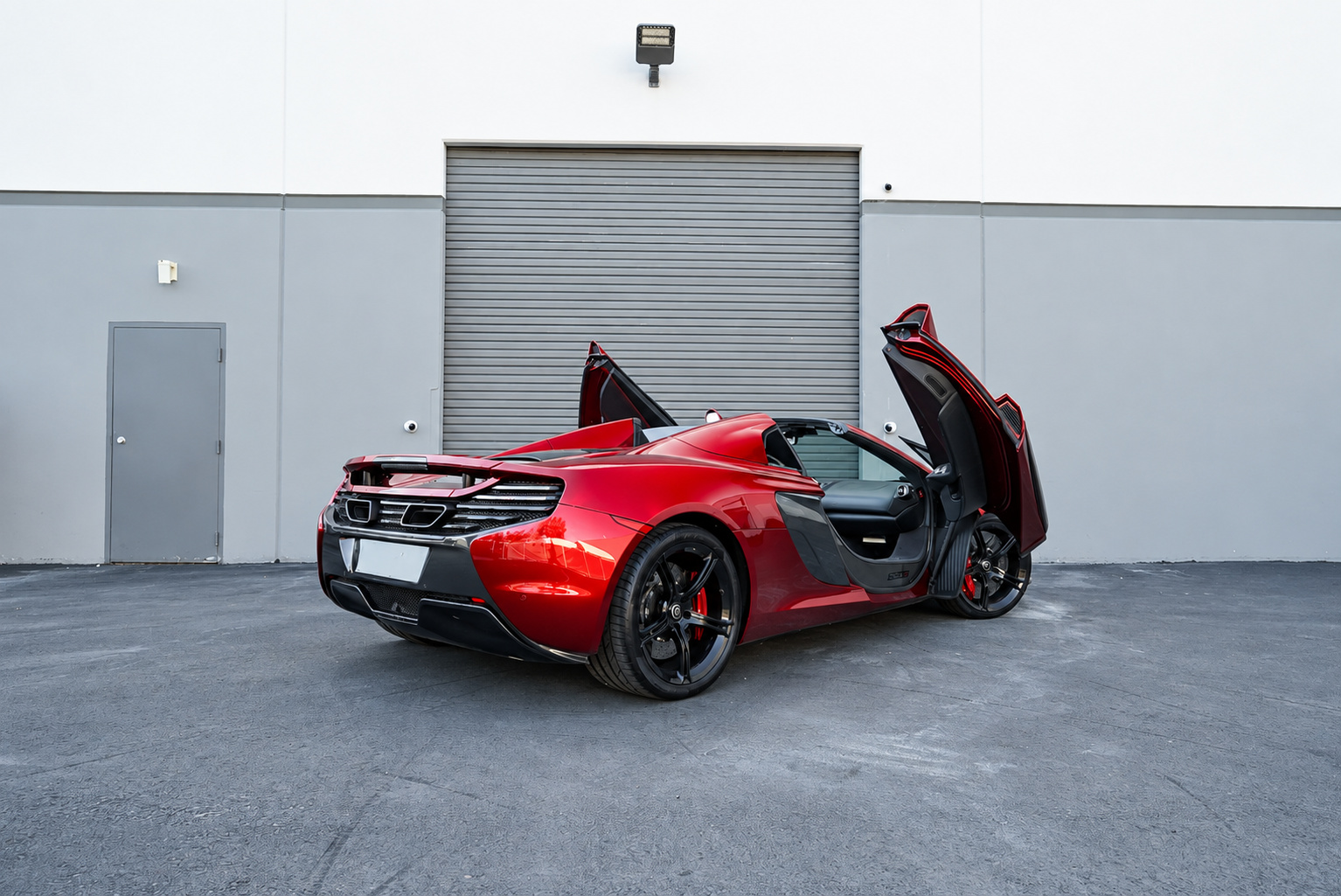 Rear three-quarter of the Volcano Red McLaren 650S Spider with both dihedral doors raised and the roof down