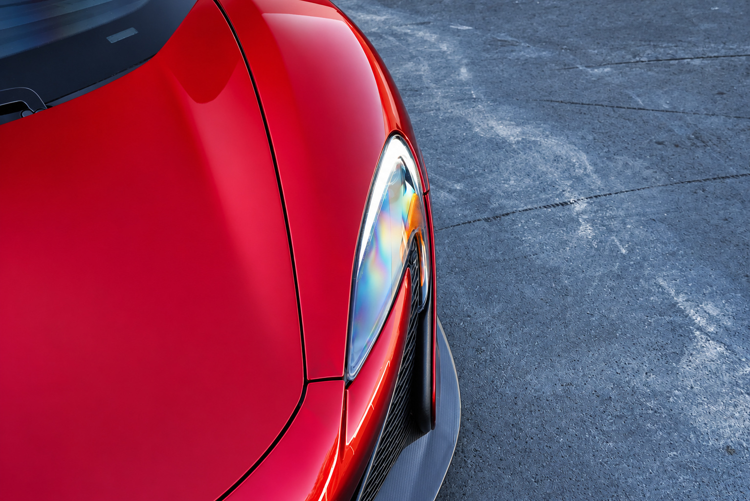 Close view of the red McLaren 650S Spider's swept headlight and the edge of the carbon splitter