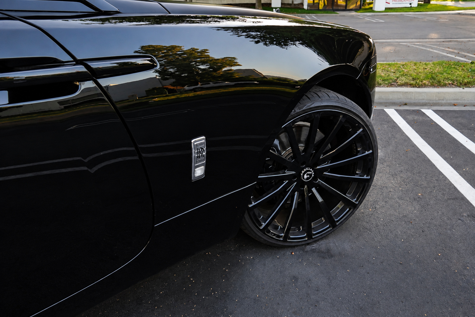 Close view of the black Wraith's rear fender and gloss black multi-spoke wheel in a parking lot
