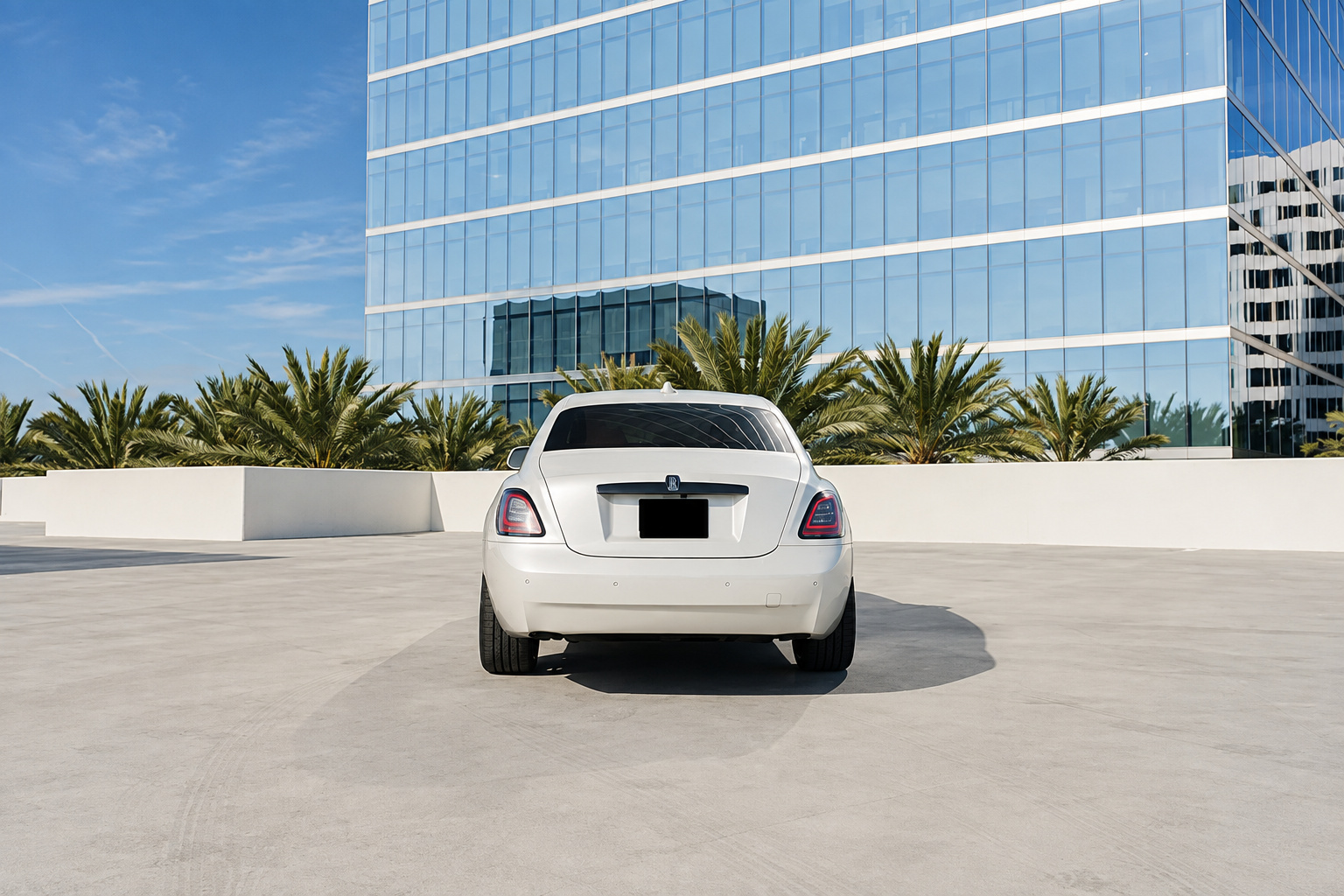 Straight rear view of the white Rolls Royce Ghost on a rooftop deck with a glass tower in the background