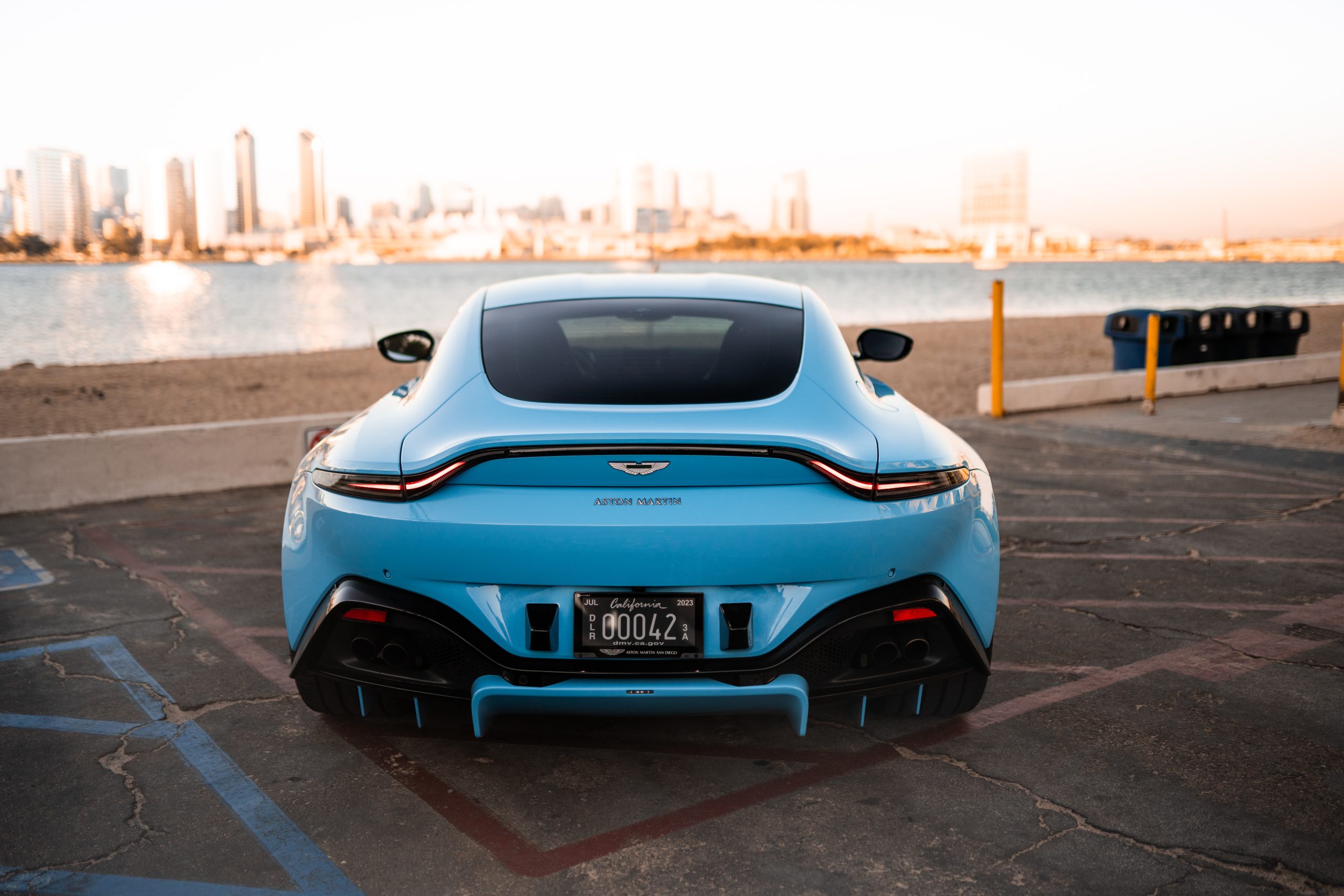Straight rear view of the baby blue Aston Martin Vantage, full-width light bar and ducktail, skyline across the bay