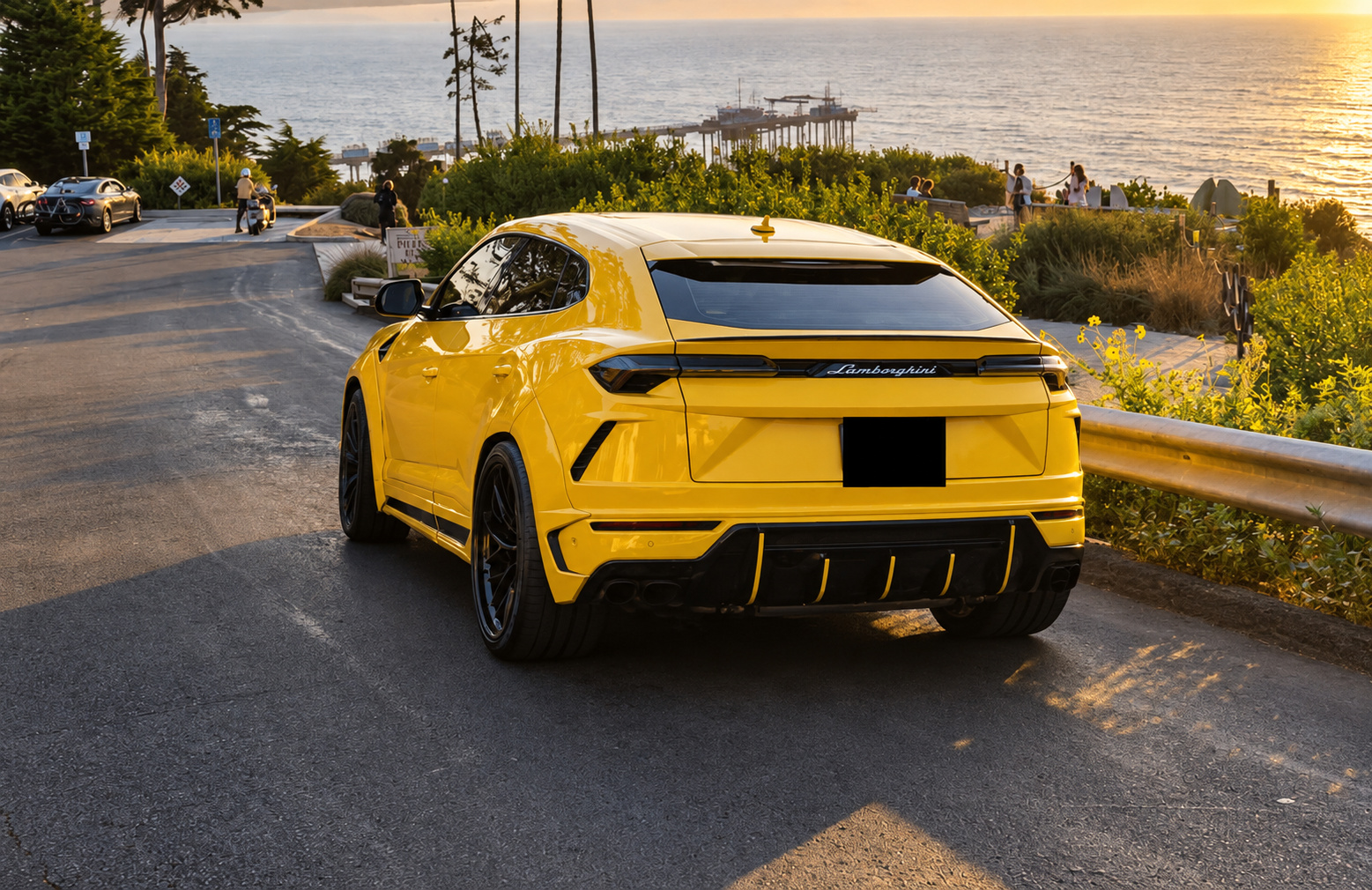 Rear three-quarter of the yellow Urus Widebody on a coastal cliff road at sunset, ocean and a pier behind