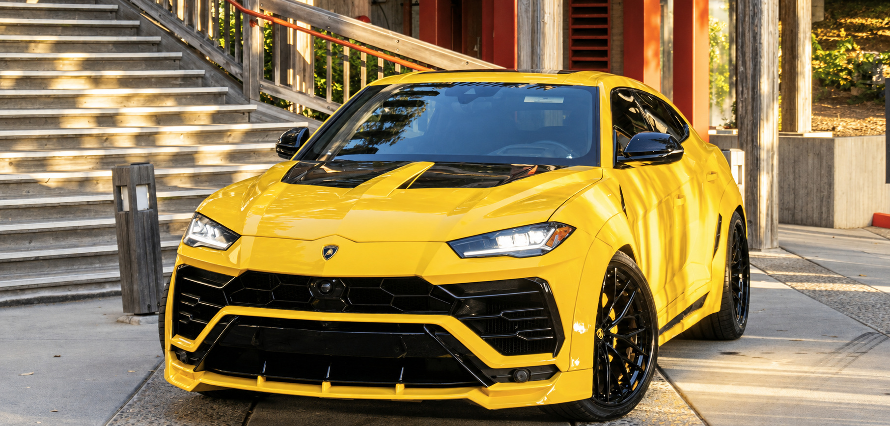 Head-on view of the yellow Urus Widebody with the black hood, Y-shaped lights and black wheels at a stair