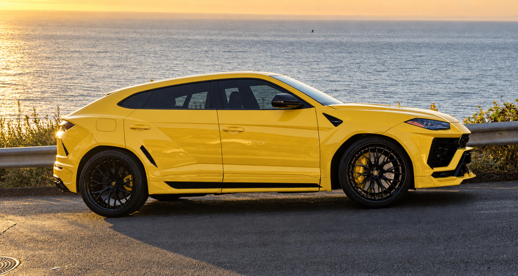 Side profile of the yellow Urus Widebody on black wheels with yellow calipers, ocean at sunset behind