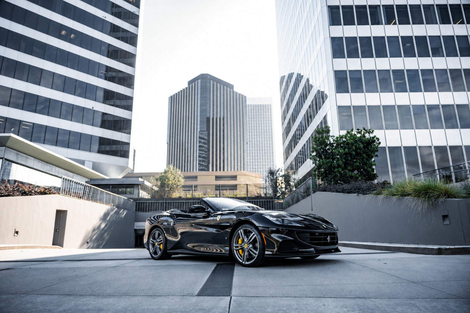 Black Ferrari Portofino with the roof down on a plaza below the glass office towers of Century City, front three-quarter