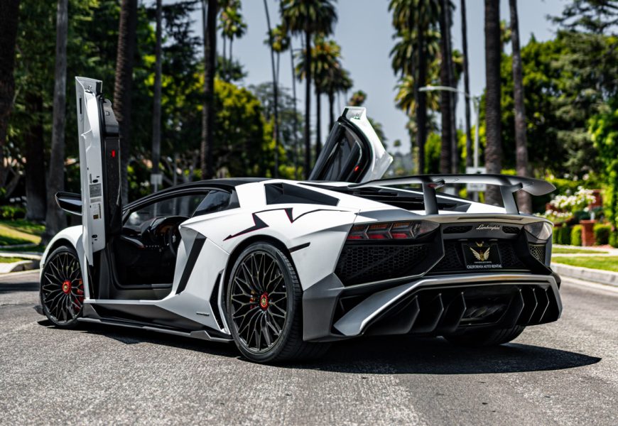 Rear three-quarter of the white Aventador SV, scissor doors up, fixed carbon wing, palms down the Beverly Hills street