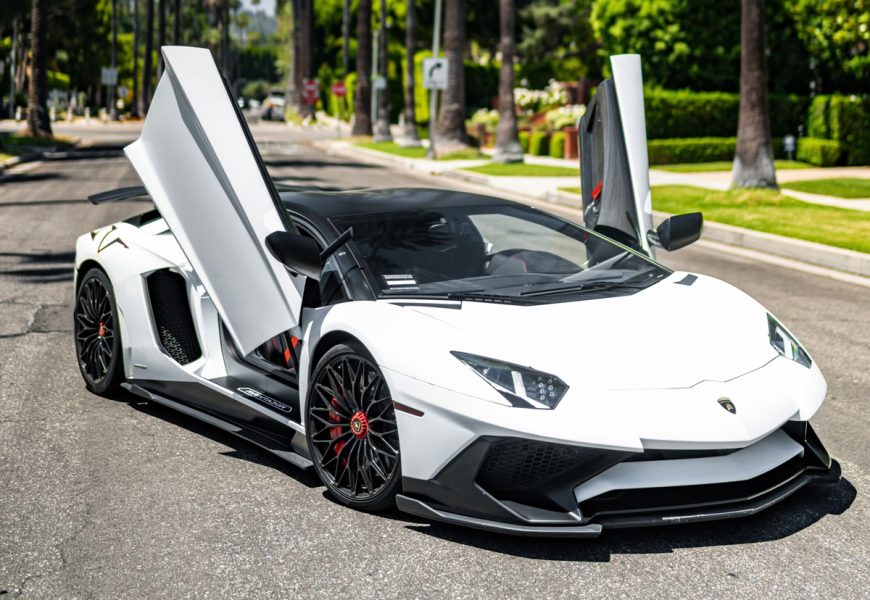 White Lamborghini Aventador SV with both scissor doors up on a palm-lined Beverly Hills street, front three-quarter